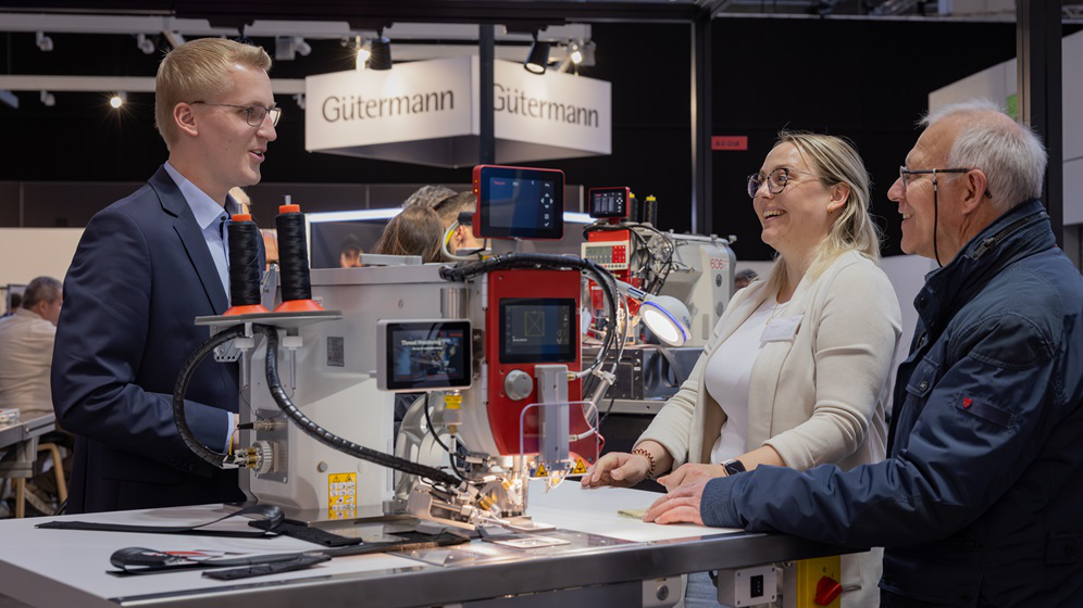 Zwei Besucher sprechen mit einem Aussteller auf einem Messestand